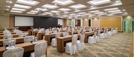 Un salón de conferencias con varias mesas y sillas, equipado con proyectores y pantallas, y piso alfombrado.