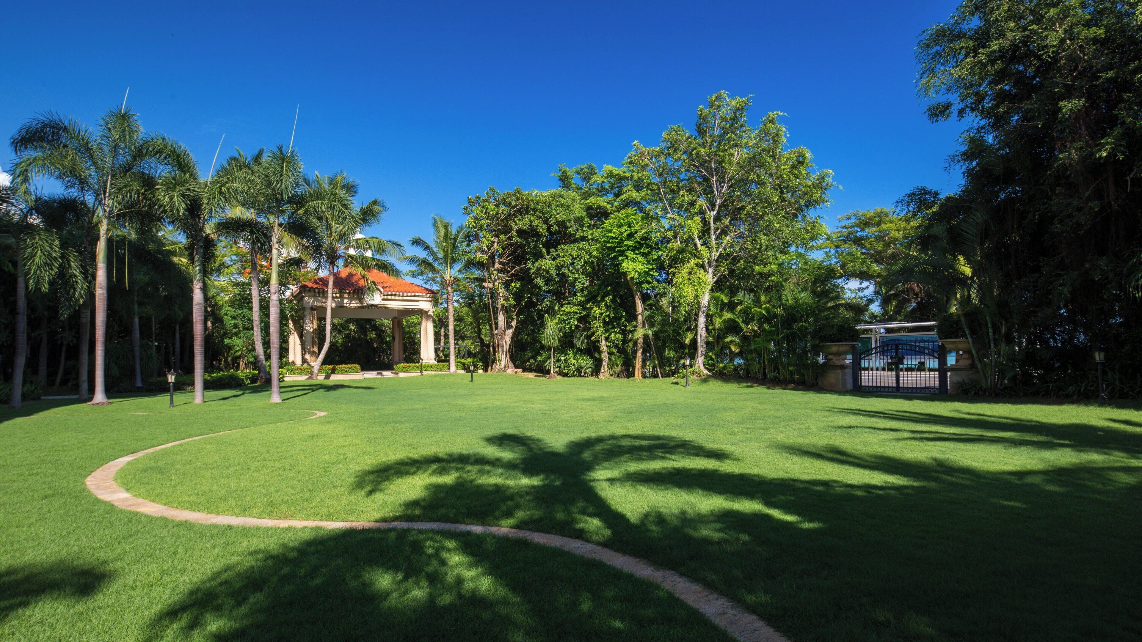 A well-maintained lawn with a gazebo, palm trees, and a building with a red roof.