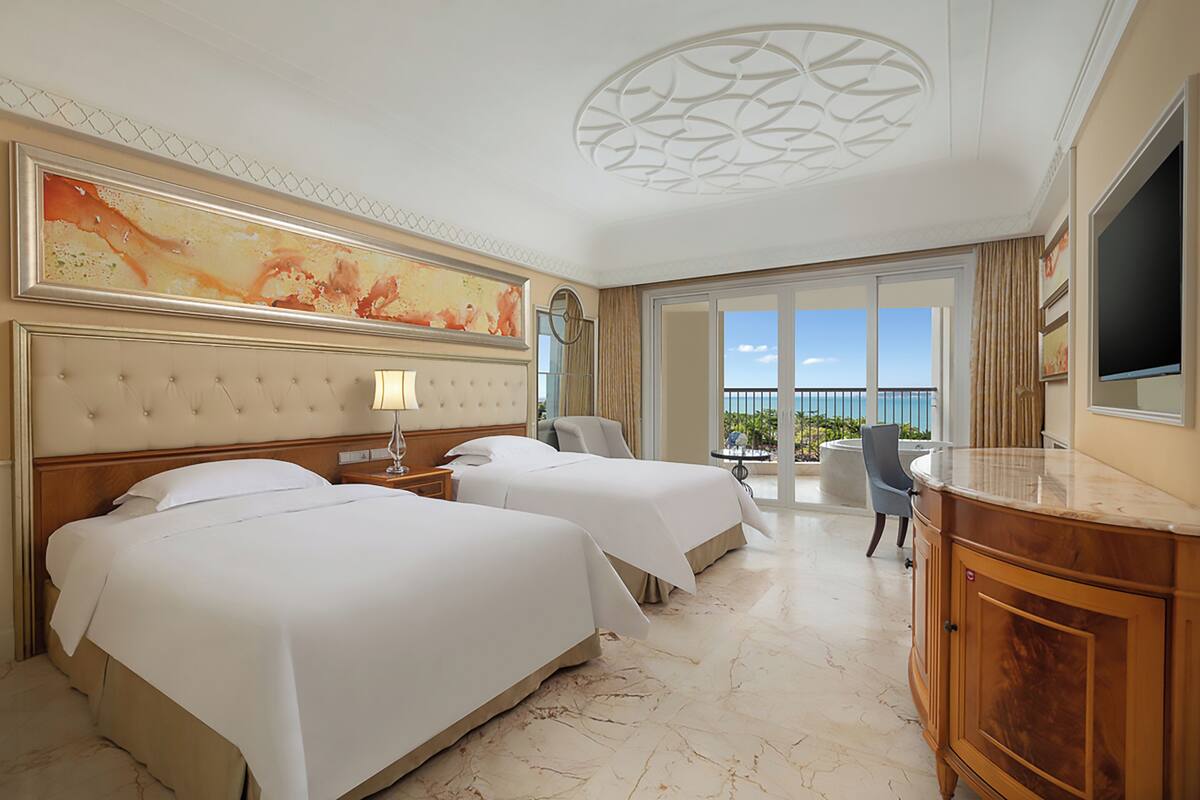 Une chambre d’hôtel avec deux lits, un grand tableau, une télévision et un balcon avec vue.