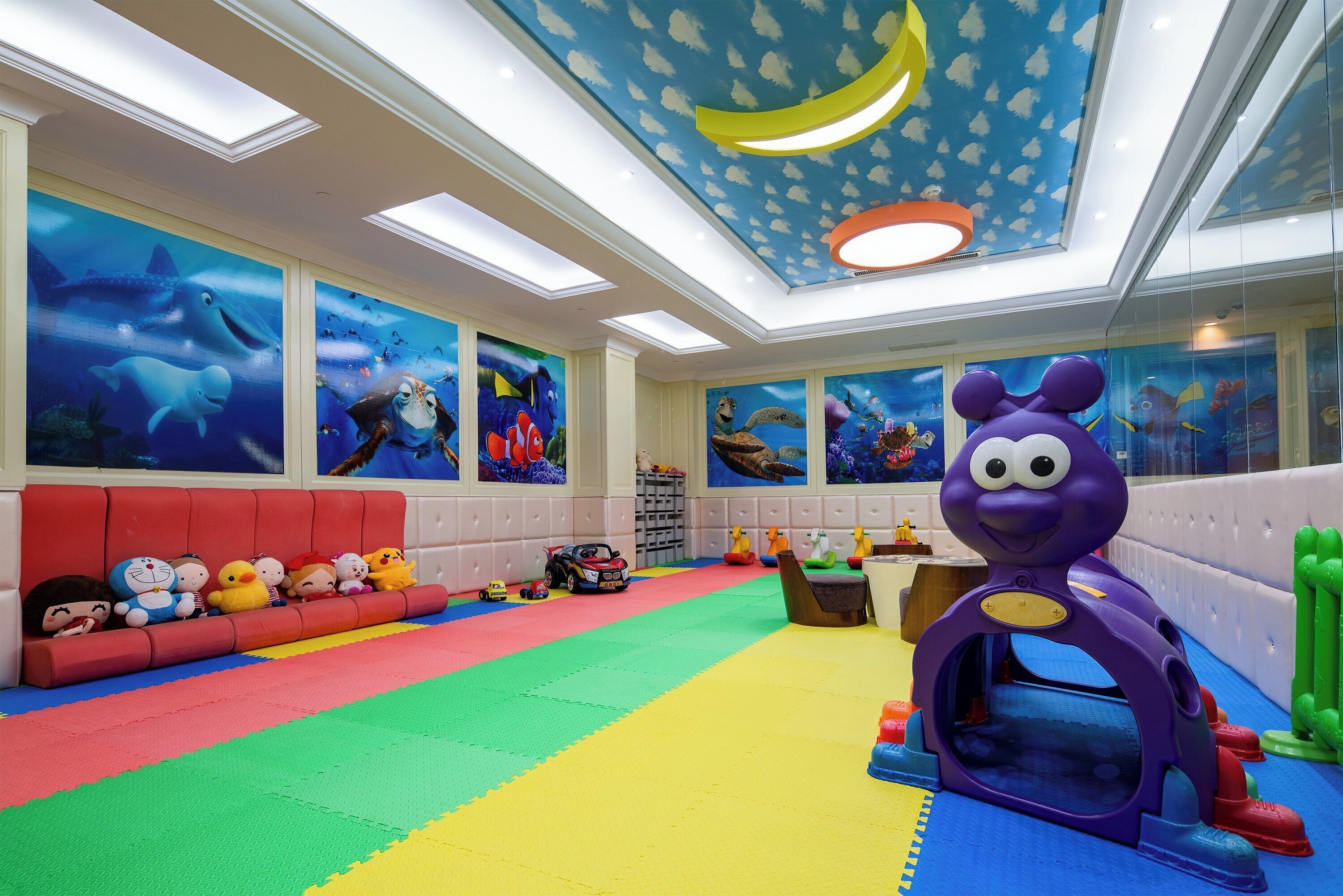 A children's play area with colorful flooring, a purple toy figure, and marine-themed wall art.