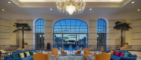 A spacious lobby with a grand chandelier, comfortable seating, and large windows offering a view of the outdoors.