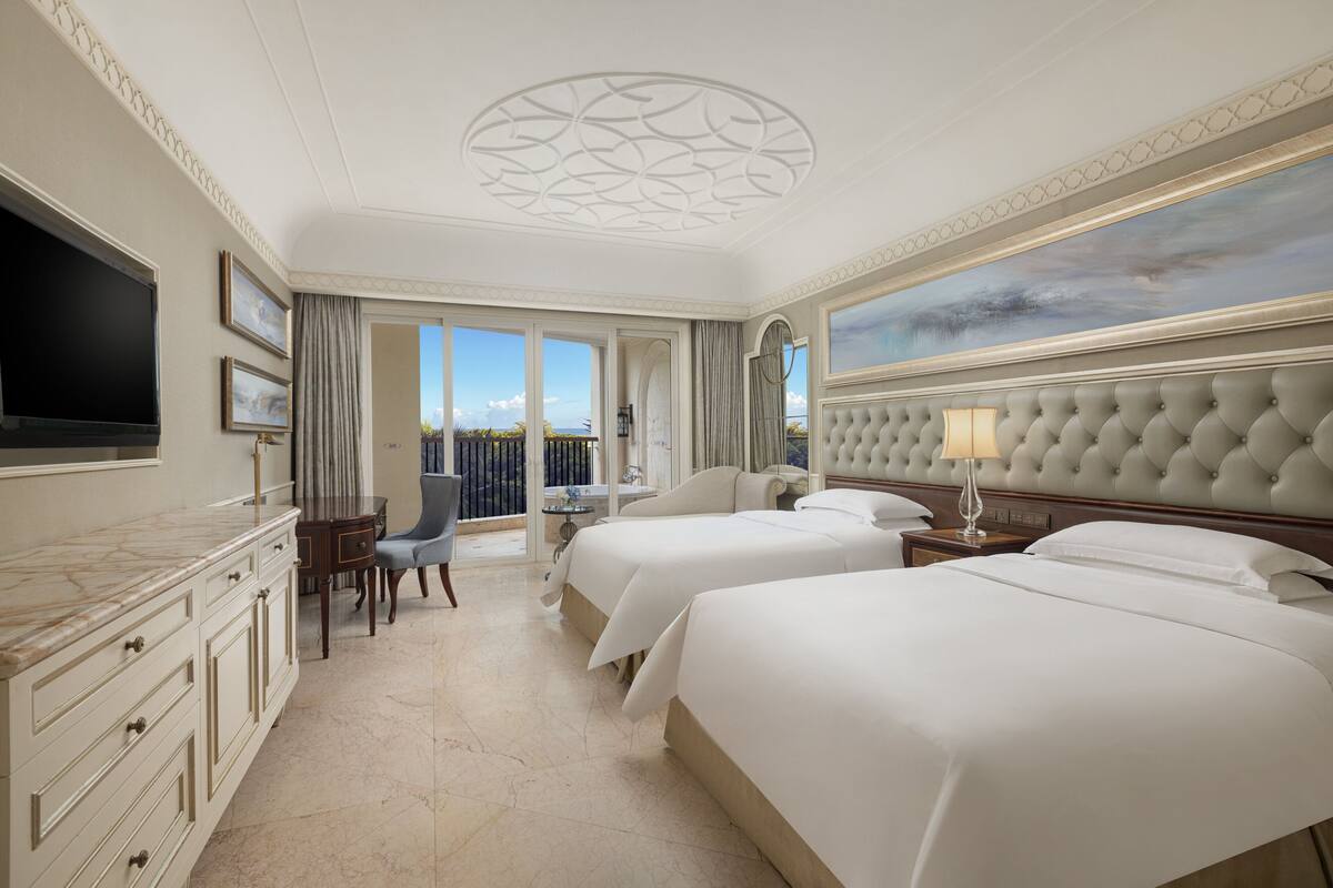 Une chambre d’hôtel avec deux lits, une télévision, un bureau avec une chaise et un balcon avec vue.
