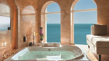 A luxurious bathroom with a large bathtub, a sofa, and a view of the sea.
