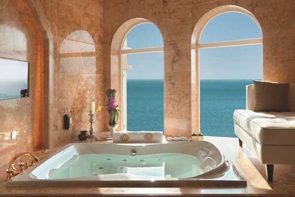 A luxurious bathroom with a large bathtub, a sofa, and a view of the sea.