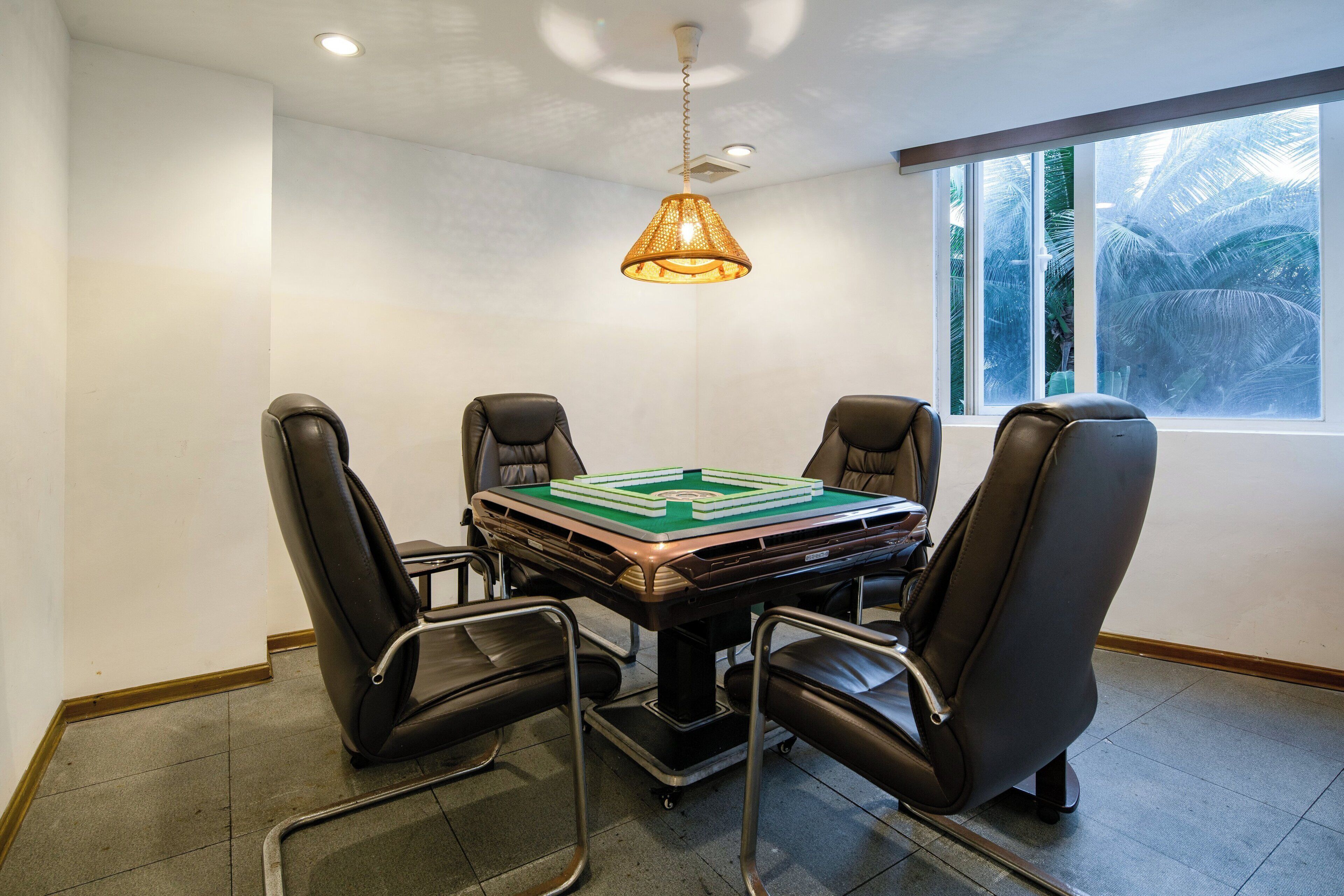 A conference room with a table, four chairs, a ceiling light, and a window with a view of palm trees.
