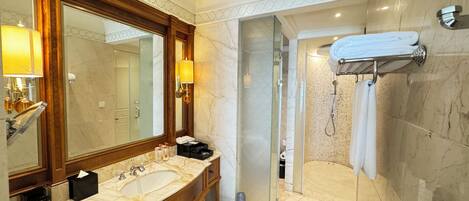 A modern bathroom with a large mirror, dual sinks, a shower with a glass door, and marble flooring.