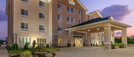 A Comfort Inn & Suites hotel with a covered entrance, multiple floors, and a landscaped front yard.