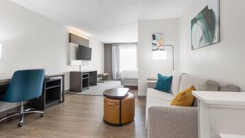 Una habitación de hotel moderna con televisión de pantalla plana, un sofá, un otoman redondos, un escritorio y una silla.