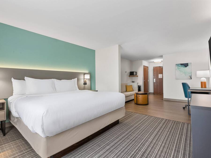 A hotel room with a bed, bedside table, lamp, desk, chair, and a television.