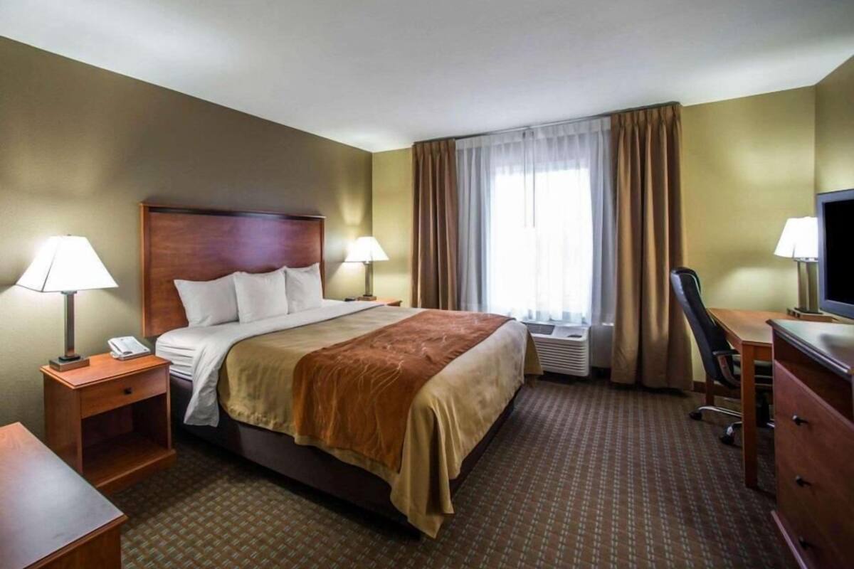 A hotel room with a bed, two bedside tables with lamps, a desk with a chair, a television, and a window with curtains.