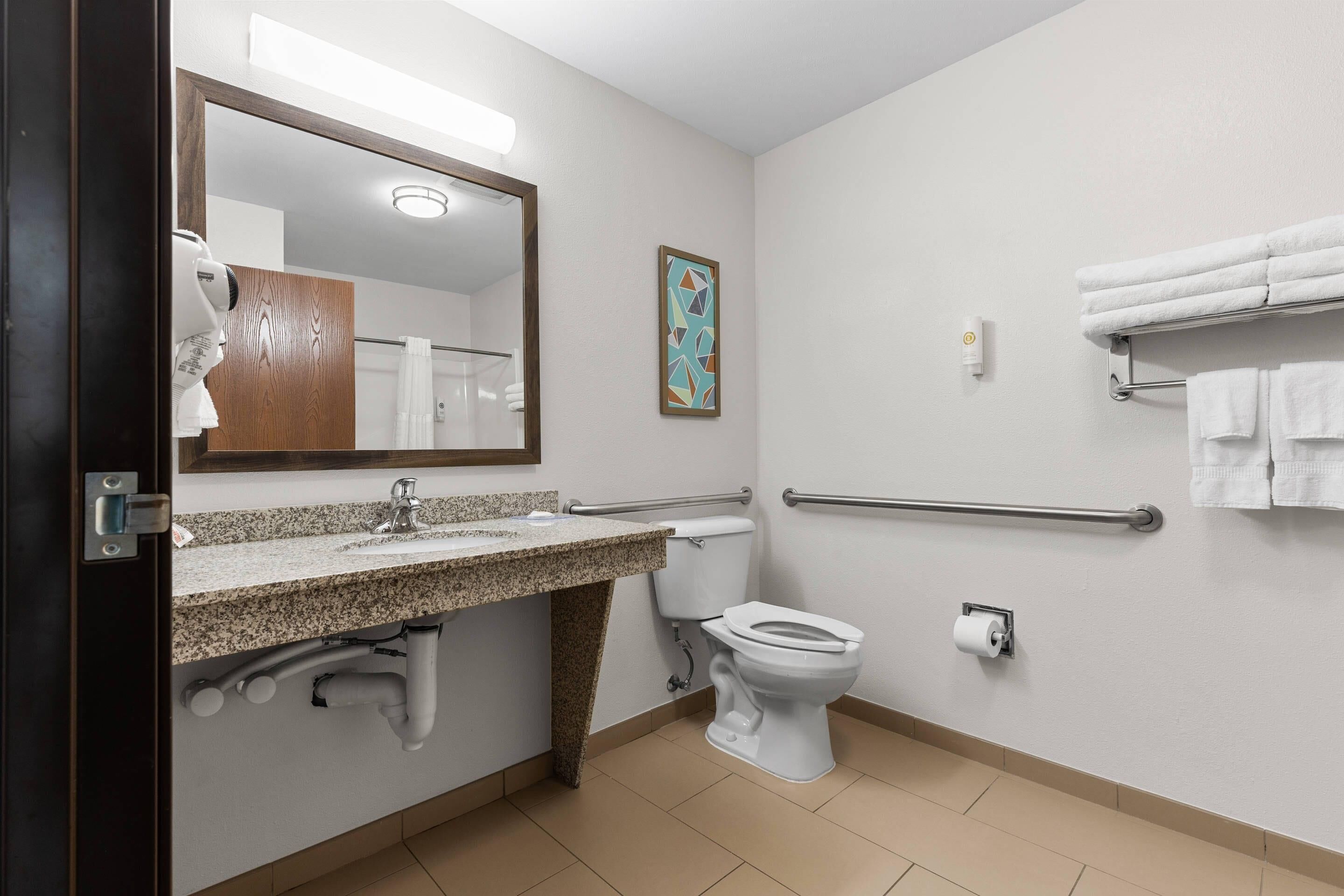 A bathroom with a sink, toilet, hand dryer, towel rack, and a mirror.