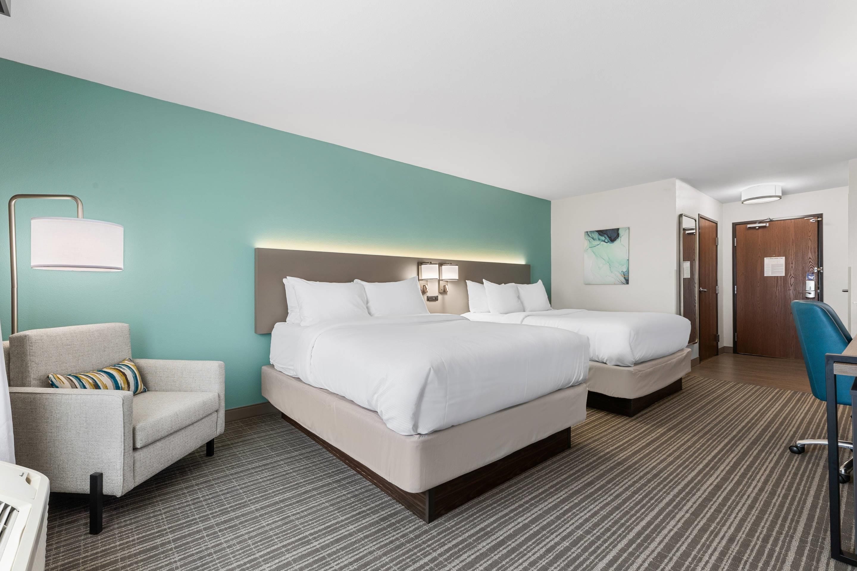 Une chambre d’hôtel avec deux lits, un bureau, une chaise, une lampe et un tableau au mur.