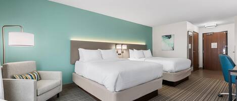 Une chambre d’hôtel avec deux lits, un bureau, une chaise, une lampe et un tableau au mur.