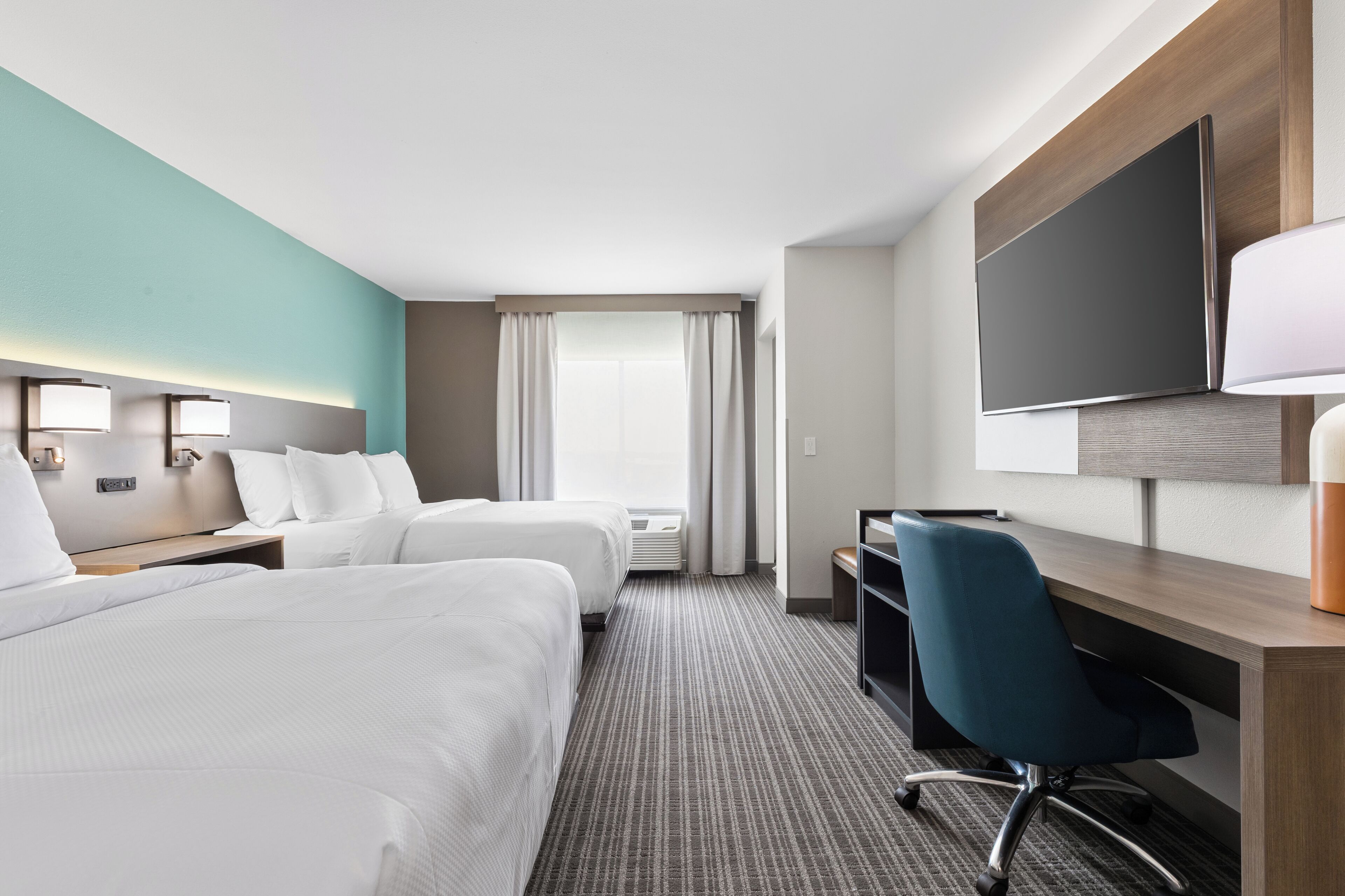 A hotel room with two beds, a desk, a chair, a TV, and a window with curtains.