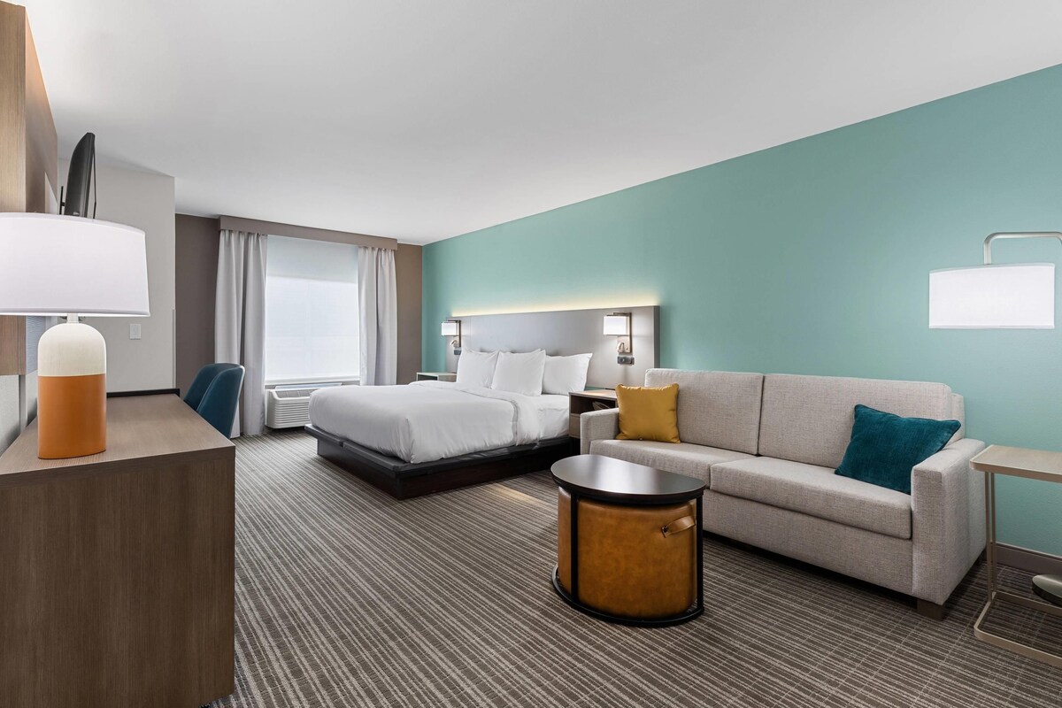 A hotel room with a bed, a sofa, a small table, a desk, and a lamp.