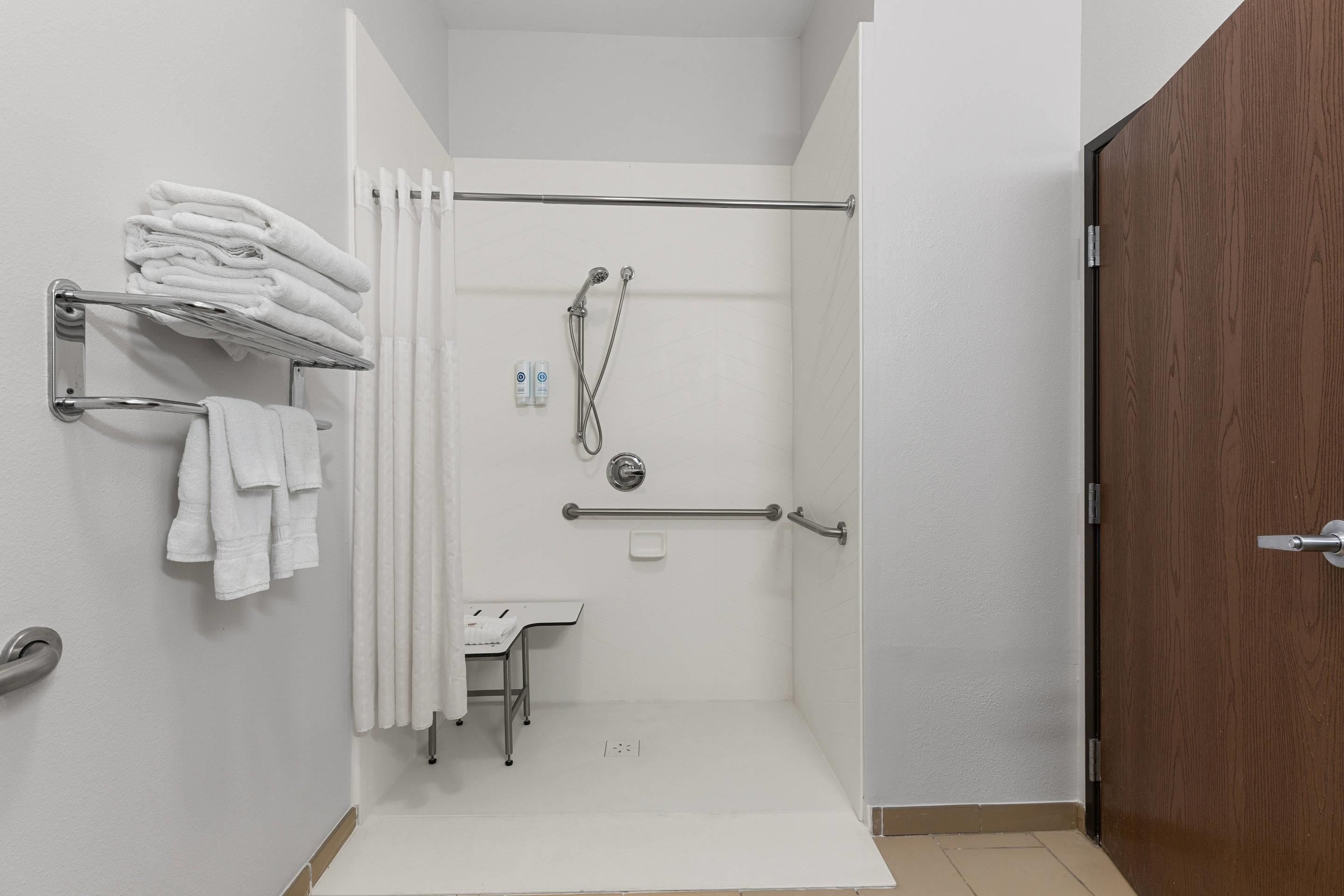 Ducha con puerta de vidrio, un perchero con toallas dobladas, una mesita y una puerta de madera.