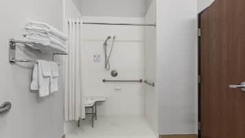 Ducha con puerta de vidrio, un perchero con toallas dobladas, una mesita y una puerta de madera.