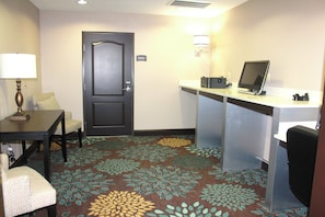 A hotel room with a desk, chair, lamp, and a door with a sign.