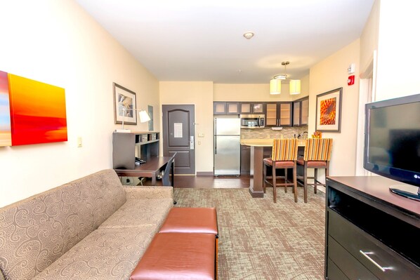 A compact living space with a sofa, a small table, a TV, and a kitchenette in the background.