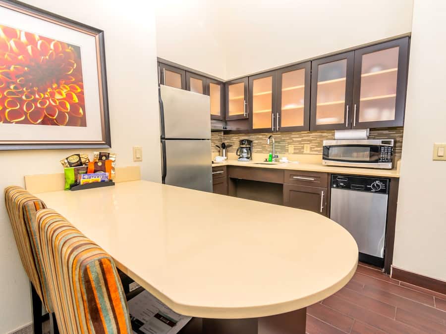 A modern kitchen with dark cabinets, a stainless steel refrigerator, a microwave, and a dishwasher.