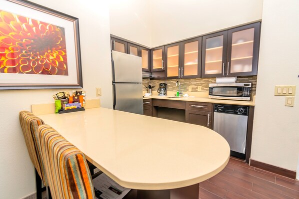 A modern kitchen with dark cabinets, a stainless steel refrigerator, a microwave, and a dishwasher.
