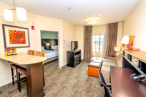 A hotel room with a dining area, a bed, a TV, a desk with a phone, and a window with curtains.