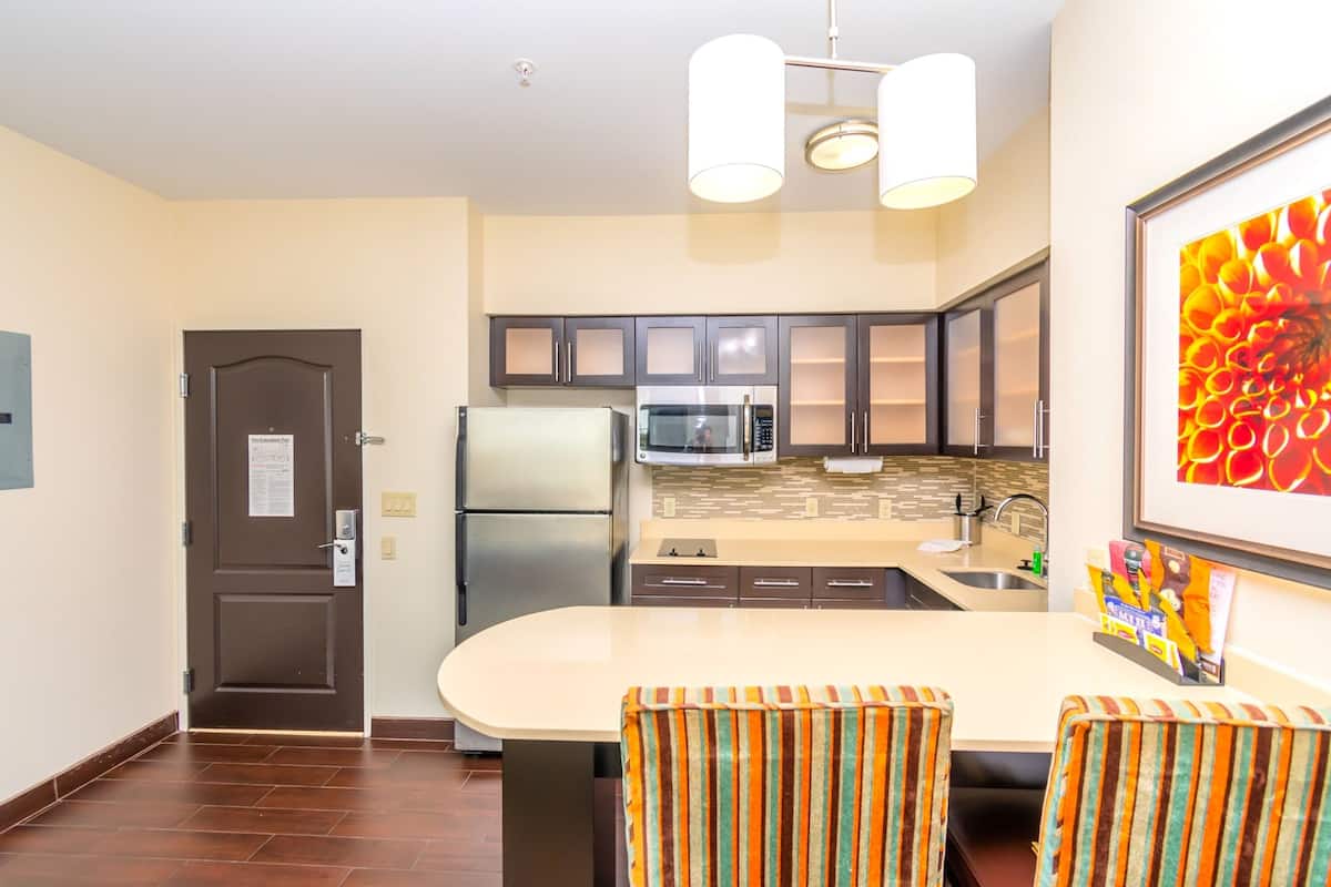 A modern kitchen with a central island, stainless steel appliances, and a dining area with striped chairs.
