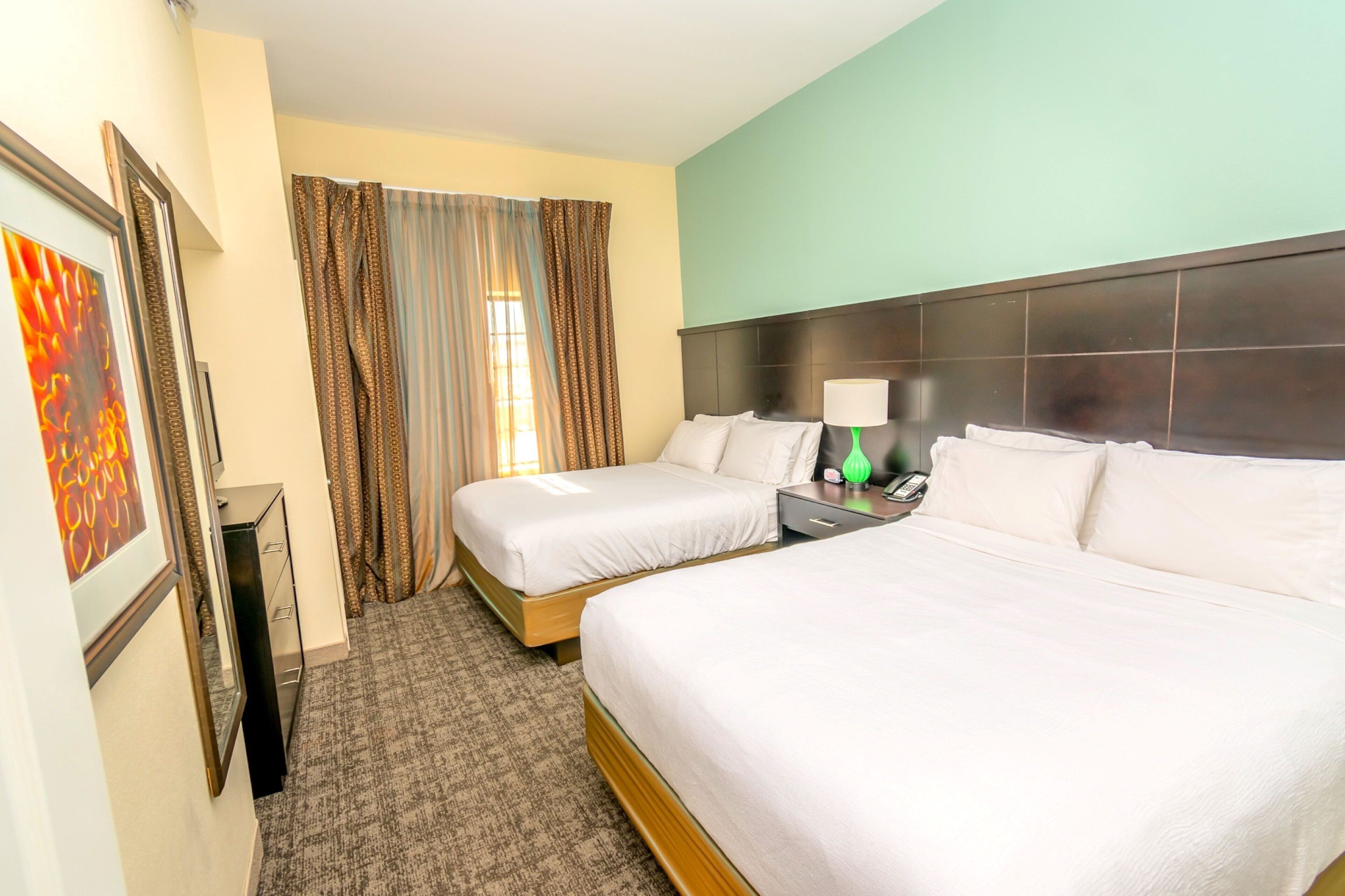A hotel room with two beds, a nightstand, a lamp, and a window with curtains.