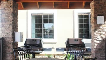 An outdoor patio with a round table and chairs, a ceiling fan, and a view of a house with large windows.