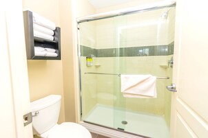 A bathroom with a glass-enclosed shower, a toilet, and a towel rack with folded towels.