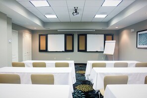 Un salón de conferencias con mesas, sillas, un proyector y pizarras.