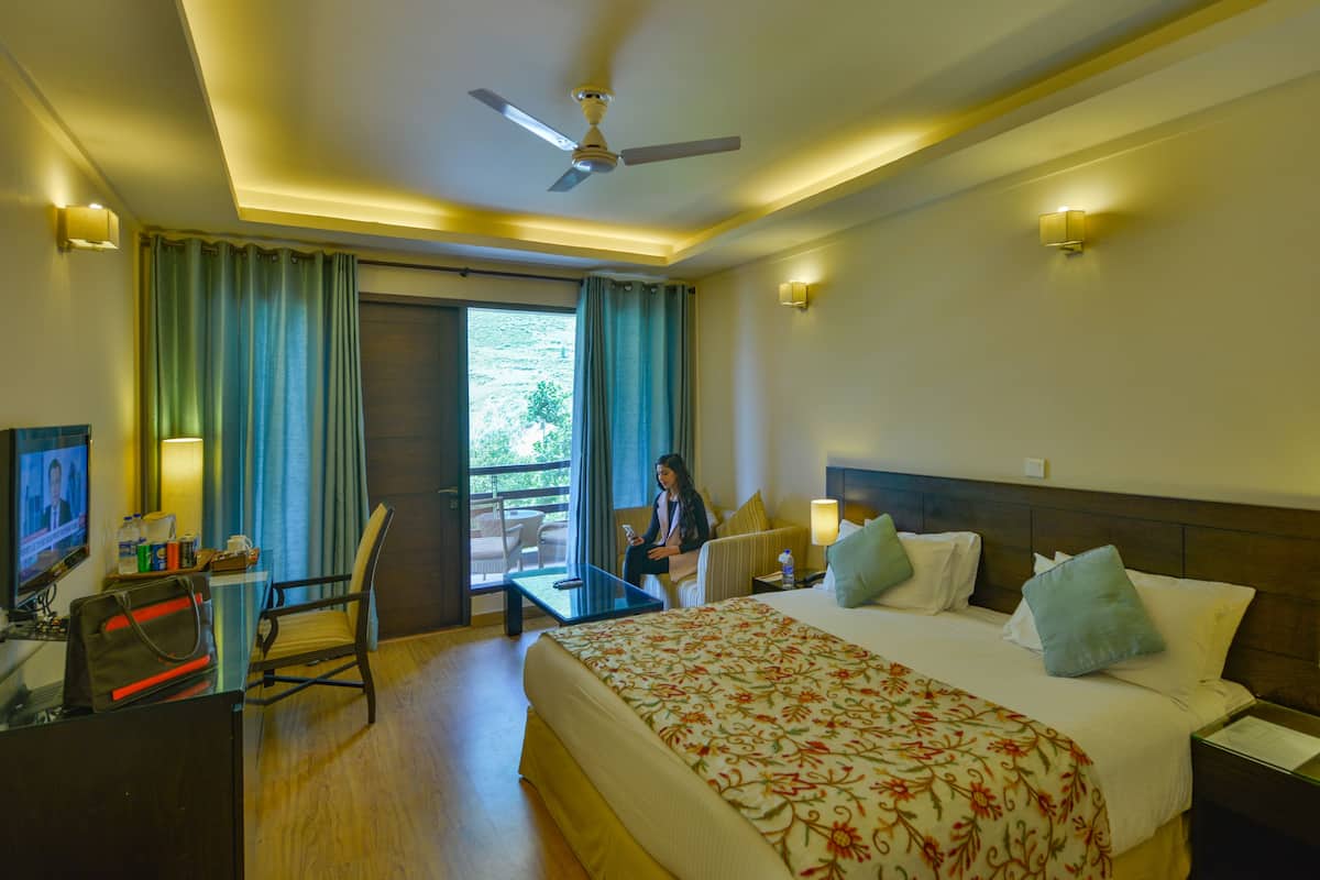 A hotel room with a bed, a desk, a chair, a television, and a balcony with curtains.