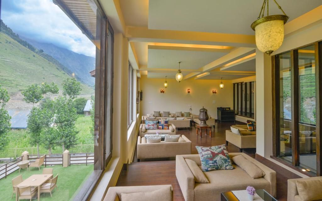 A spacious living area with multiple sofas and a television, large windows offering a view of a green landscape, and a balcony with outdoor seating.