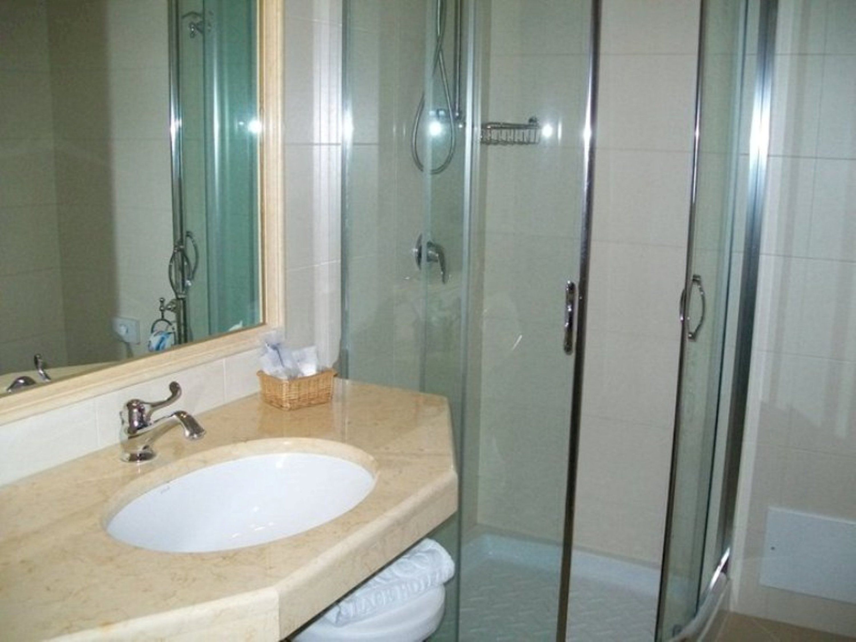 Een badkamer met een douche met glazen wand, een wastafel met spiegel, en een mandje met toiletartikelen.