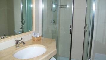 Een badkamer met een douche met glazen wand, een wastafel met spiegel, en een mandje met toiletartikelen.