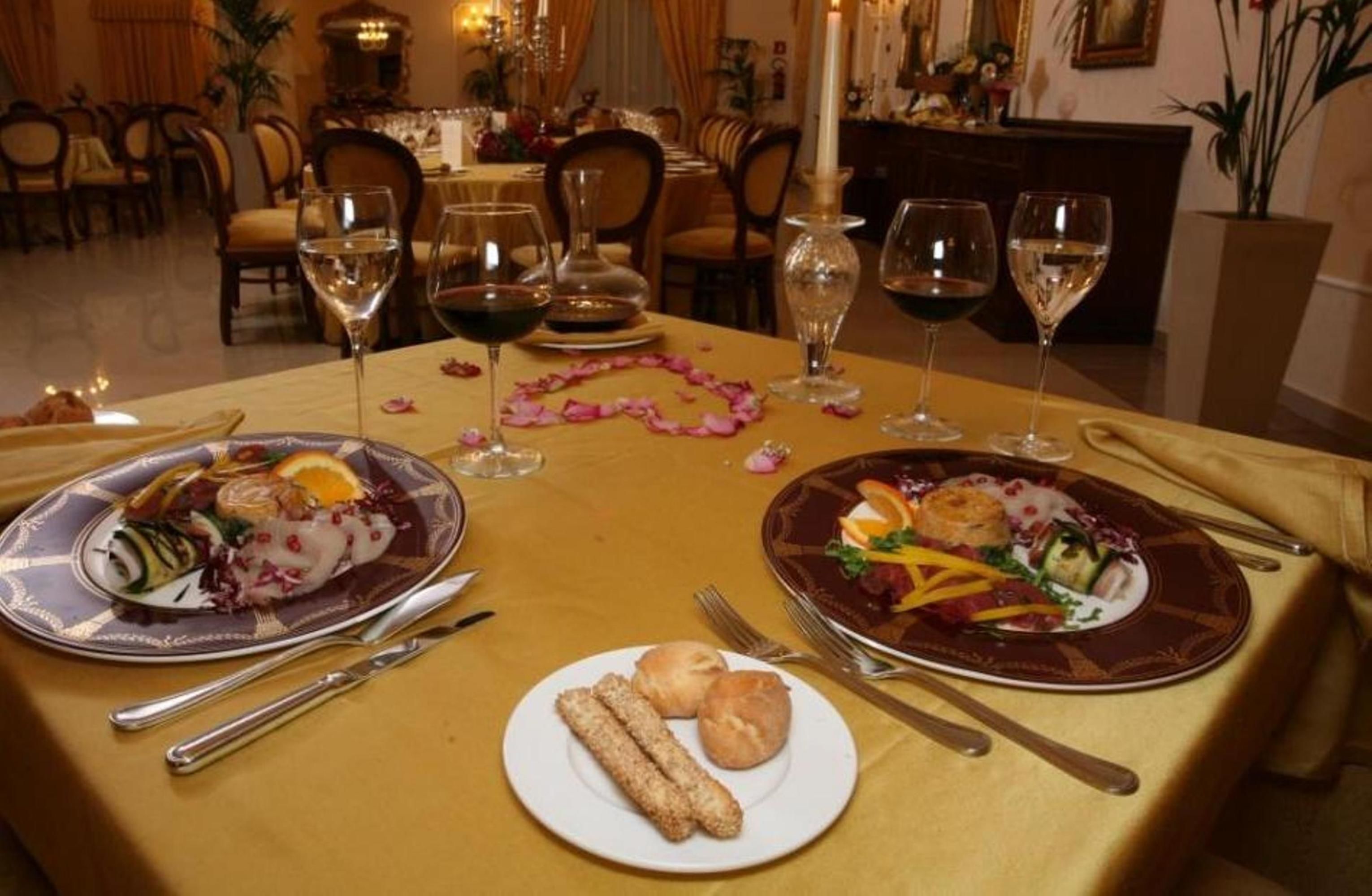 A dining table set with two plates of food, wine glasses, and cutlery.