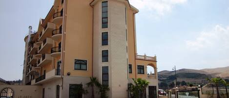 A multi-story hotel with a swimming pool, balconies, and a view of the surrounding landscape.