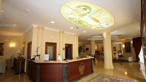 Un vestíbulo de hotel con un mostrador de recepción, una lámpara de araña grande y una alfombra estampada.