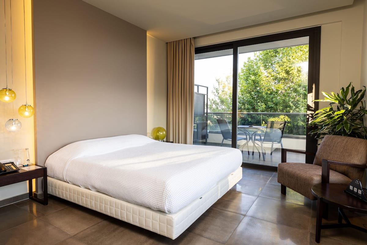 Una habitación de hotel moderna con una cama grande, un escritorio, una silla y un balcón con mobiliario exterior.