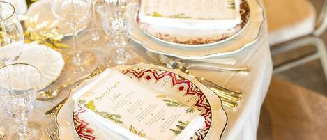 A table set for a formal event with white tablecloths, gold-rimmed plates, and clear glassware.