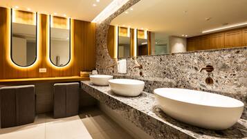 A modern bathroom with two large white sinks, a granite countertop, and a large mirror with integrated lighting.