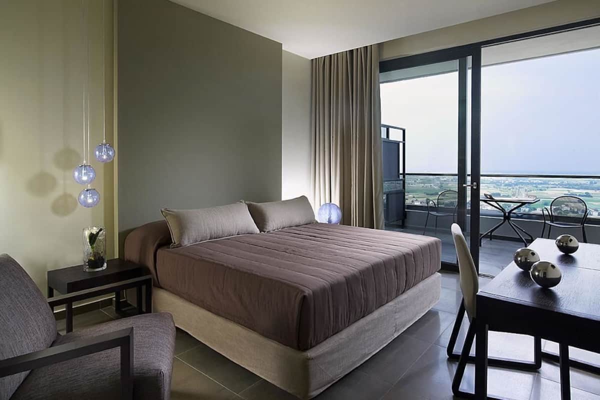 Una habitación de hotel moderna con una cama grande, una mesa de comedor y un balcón con vistas a la ciudad.