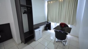 A modern room with a built-in wardrobe, a small refrigerator, a dining table with two chairs, and a window with curtains. - Hotel Fit (Palmas)