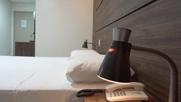 A hotel room with a bed, a bedside lamp, a telephone, and a wall-mounted air conditioner. - Hotel Fit (Palmas)