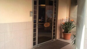Ein Hotel Eingang mit Glastür, einem Sicherheitstastaturfeld und einem Blumentopf mit orangefarbenen Blüten.