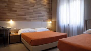 Ein Hotelzimmer mit einem hölzernen Kopfende, einem Bett mit orangefarbener Bettdecke, einem Nachttisch mit Lampe und einem Fenster mit Vorhängen.