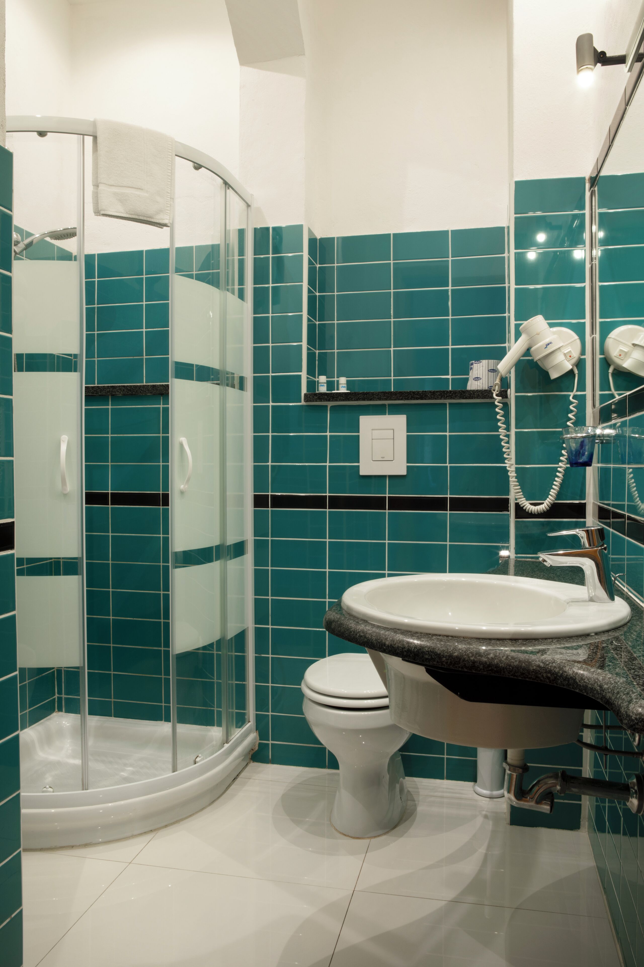 Een badkamer met een douchecabine van glas, een wit toilet en een wastafel met een granieten aanrecht.