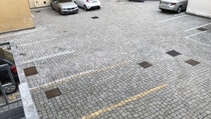 Ein Parkplatz mit Kopfsteinpflasterbelag, gekennzeichneten Stellplätzen und einem Metallgitter.