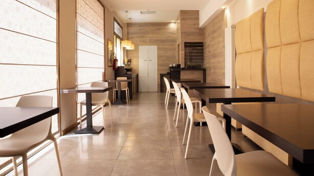 Ein modernes Restaurantambiente mit hohen Tischen und Stühlen, einer Wand in Holzoptik und Blick in die Küche.