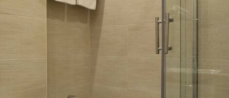 Un baño moderno con ducha envuelta en vidrio, lavamanos pedestal y un inodoro.
